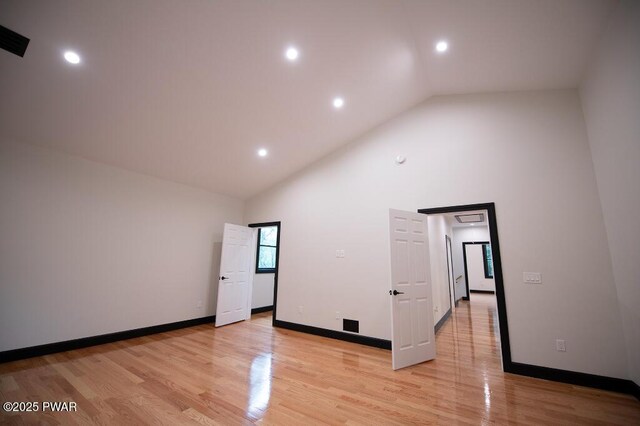 empty room with recessed lighting, baseboards, light wood finished floors, and high vaulted ceiling