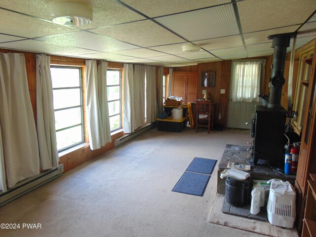 miscellaneous room featuring a baseboard radiator, a wood stove, a drop ceiling, and wooden walls