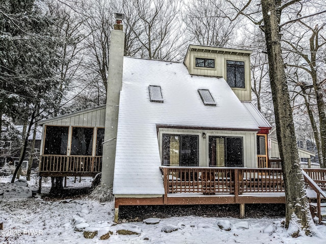 snow covered back of property featuring a sunroom