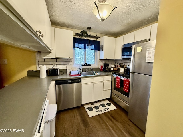 kitchen with appliances with stainless steel finishes, sink, white cabinets, hanging light fixtures, and dark wood-type flooring