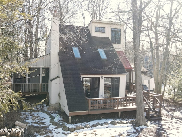 snow covered rear of property with a deck and a sunroom