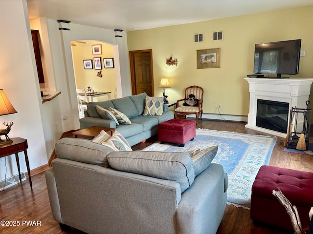 living area featuring visible vents, dark wood finished floors, a baseboard radiator, arched walkways, and a glass covered fireplace