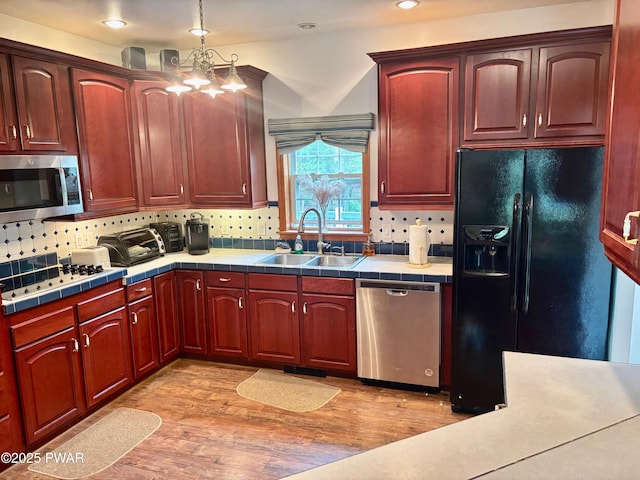 kitchen with appliances with stainless steel finishes, dark brown cabinets, tile counters, and a sink