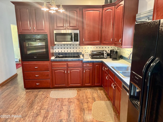 kitchen with black appliances, light wood-style floors, tasteful backsplash, and a toaster