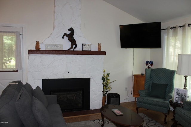 living room with a stone fireplace, wood-type flooring, and lofted ceiling