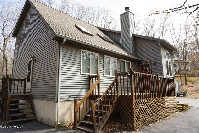 back of house with a chimney, roof with shingles, and a deck