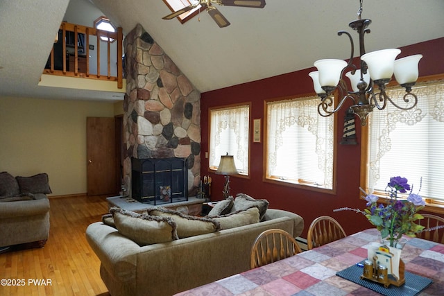 living room with a stone fireplace, high vaulted ceiling, wood finished floors, and ceiling fan with notable chandelier