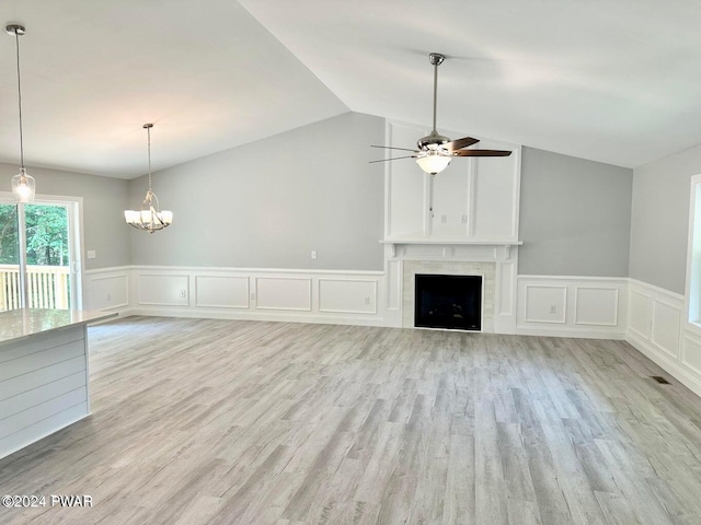 unfurnished living room with a tiled fireplace, ceiling fan with notable chandelier, vaulted ceiling, and light hardwood / wood-style floors