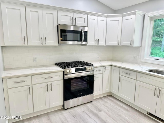 kitchen with decorative backsplash, appliances with stainless steel finishes, light hardwood / wood-style flooring, and white cabinets