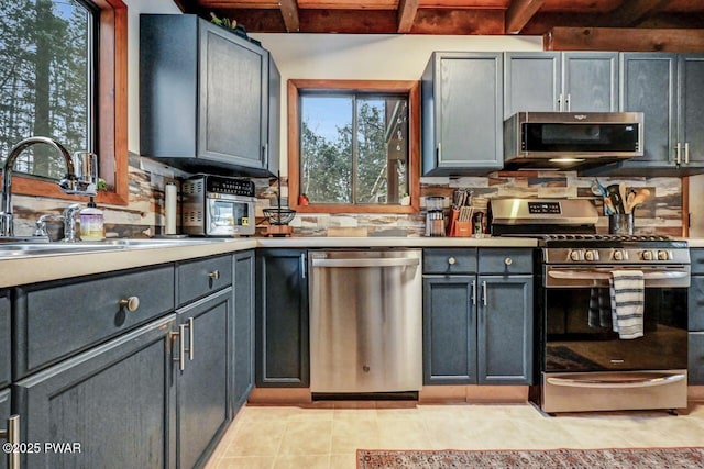 kitchen with sink, gray cabinetry, light tile patterned floors, appliances with stainless steel finishes, and beamed ceiling