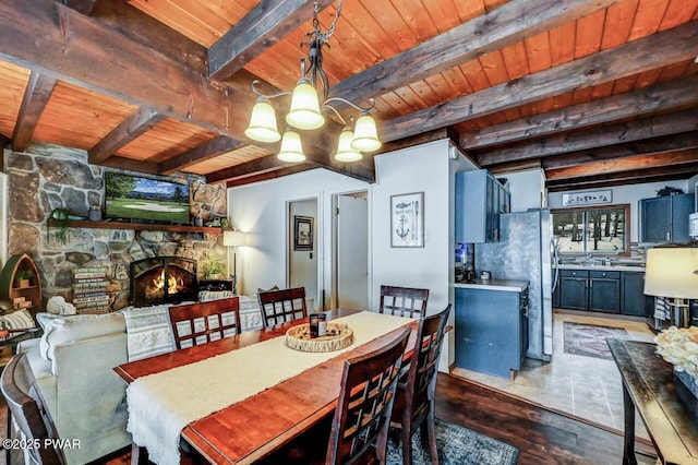 dining room featuring a stone fireplace, a chandelier, beam ceiling, and wooden ceiling