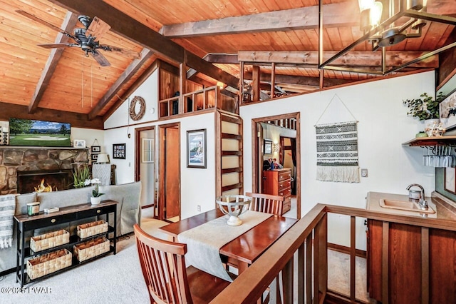 carpeted dining space with vaulted ceiling with beams, a stone fireplace, sink, and wooden ceiling