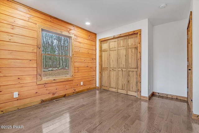 unfurnished bedroom with wooden walls, a closet, and wood-type flooring