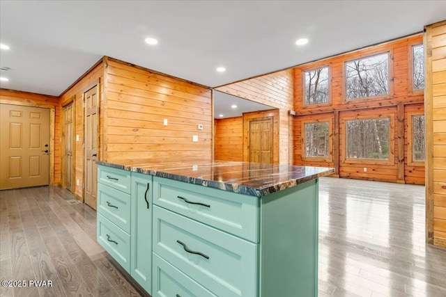 kitchen with light wood-type flooring, wooden walls, dark stone countertops, a center island, and green cabinets