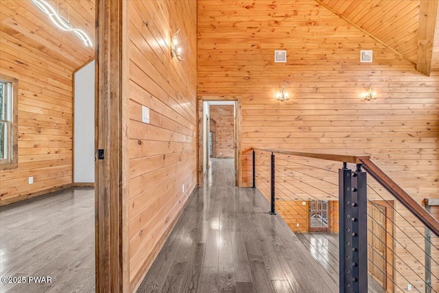 hall with wood walls, wood-type flooring, and high vaulted ceiling