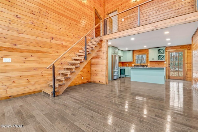 unfurnished living room with hardwood / wood-style floors, a towering ceiling, and wooden walls