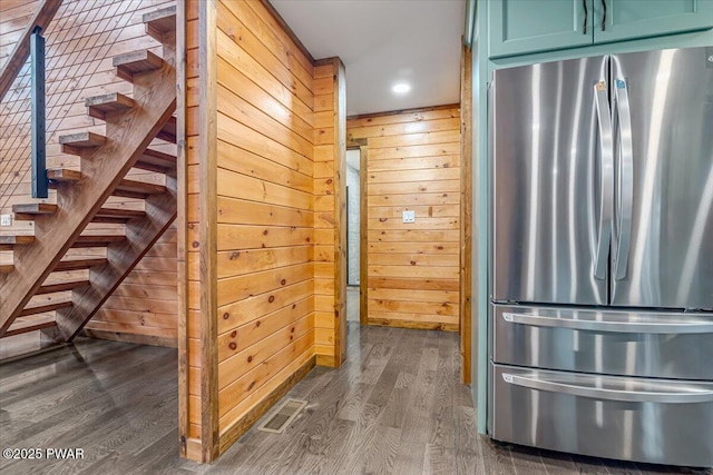 interior space with wood walls, dark hardwood / wood-style flooring, stainless steel fridge, and green cabinets