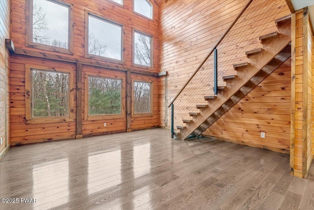 unfurnished living room featuring hardwood / wood-style floors, a towering ceiling, and wooden walls