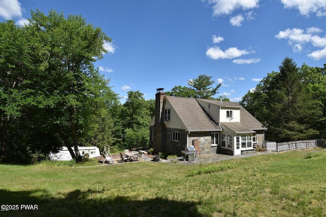 rear view of property featuring stone siding, a yard, a chimney, and fence