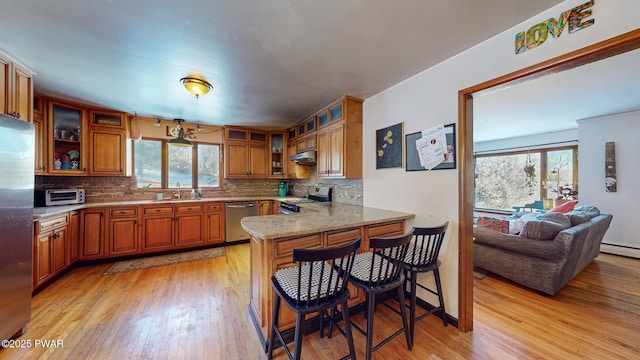 kitchen featuring appliances with stainless steel finishes, glass insert cabinets, a breakfast bar area, a peninsula, and light stone countertops