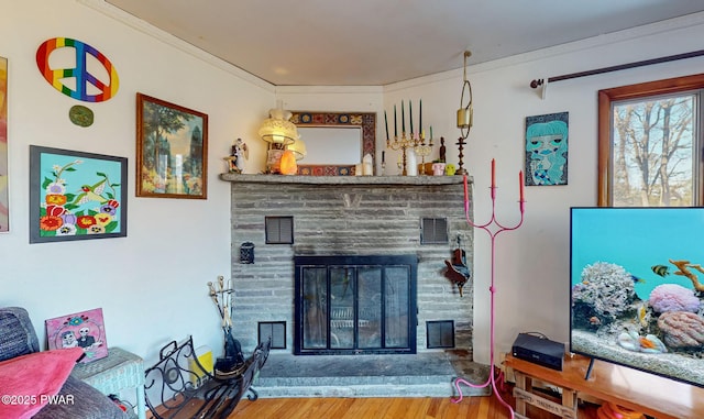 living room featuring a stone fireplace, wood finished floors, and crown molding