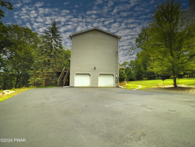 exterior space with aphalt driveway, stairway, an attached garage, and a yard