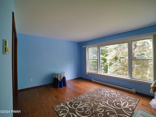 unfurnished room featuring a baseboard heating unit, hardwood / wood-style flooring, and baseboards