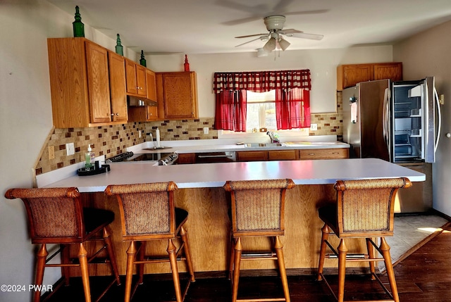 kitchen featuring a kitchen bar, decorative backsplash, kitchen peninsula, ceiling fan, and sink