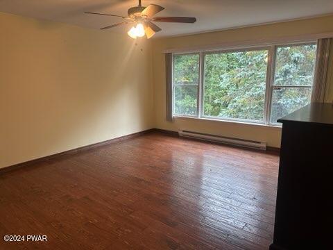 spare room featuring a baseboard radiator, baseboards, wood finished floors, and a ceiling fan