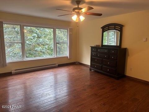 unfurnished bedroom with dark wood-type flooring, ceiling fan, and a baseboard heating unit