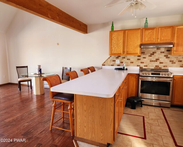 kitchen with decorative backsplash, ceiling fan, stainless steel range oven, beamed ceiling, and a breakfast bar area