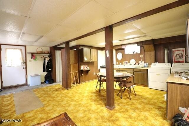 dining room with washer / dryer, light colored carpet, a drop ceiling, and wooden walls