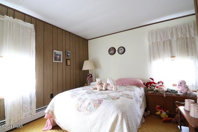 bedroom with a baseboard radiator, light colored carpet, and wood walls