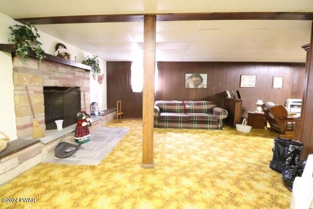 carpeted living room with beam ceiling, wooden walls, and a fireplace