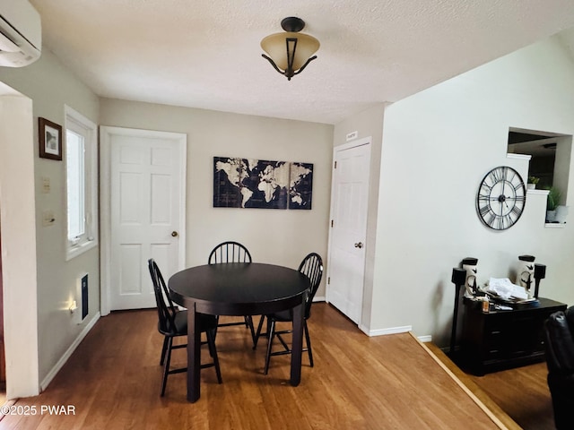 dining space with a wall mounted air conditioner, baseboards, and wood finished floors