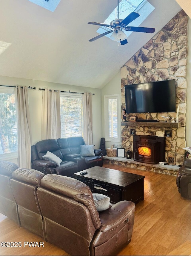 living room featuring ceiling fan, vaulted ceiling, wood finished floors, and a stone fireplace