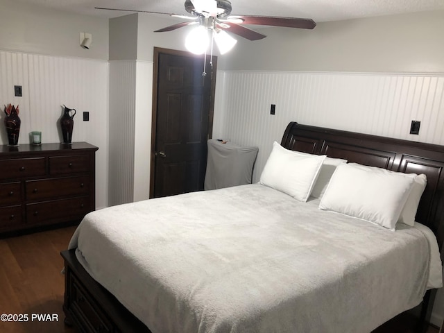 bedroom with a wainscoted wall, dark wood finished floors, and a ceiling fan