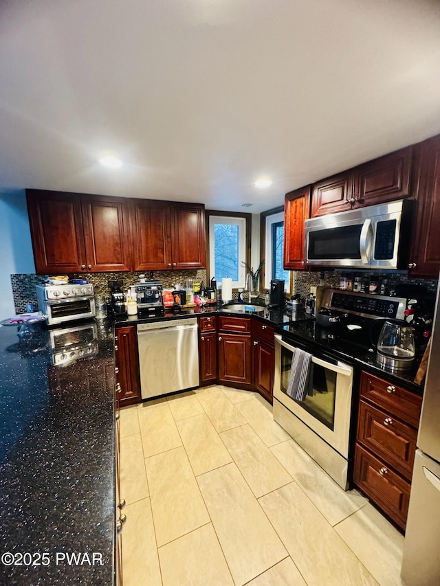 kitchen with dark stone counters, backsplash, stainless steel appliances, dark brown cabinets, and a sink