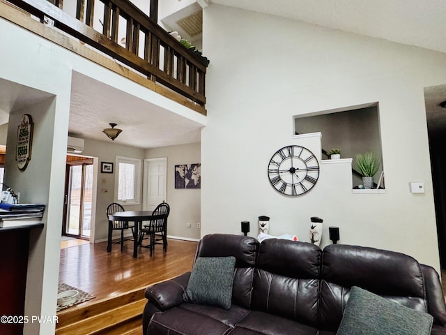 living area with high vaulted ceiling, a wall mounted air conditioner, wood finished floors, and baseboards