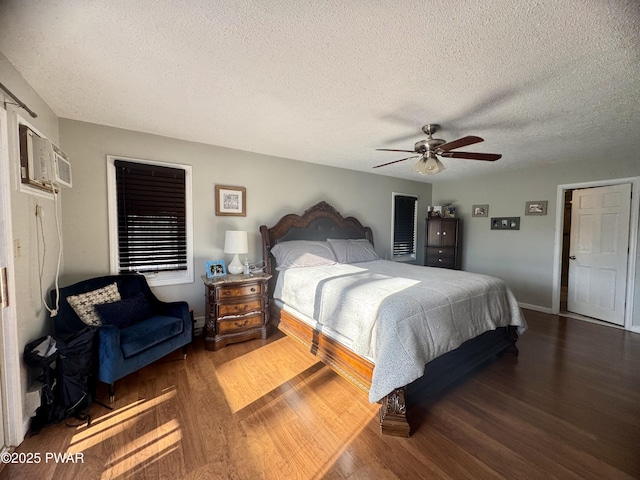 bedroom featuring a textured ceiling, dark wood-type flooring, a ceiling fan, baseboards, and a wall mounted air conditioner