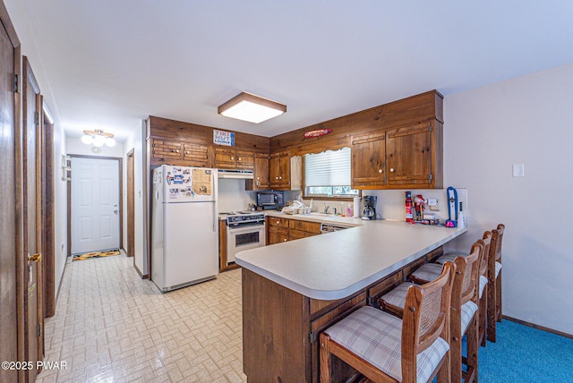 511 Overlook Ter, Stroudsburg, PA 18360 - kitchen with white appliances, a peninsula, brown cabinetry, under cabinet range hood, and a kitchen breakfast bar