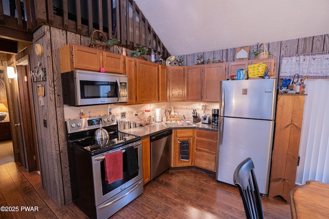 kitchen featuring brown cabinetry, appliances with stainless steel finishes, dark wood-style flooring, a textured ceiling, and a sink