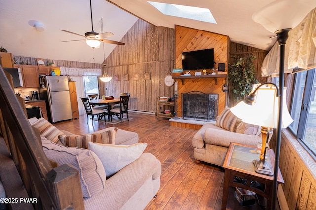 living area with ceiling fan, a fireplace with raised hearth, wooden walls, a skylight, and wood-type flooring