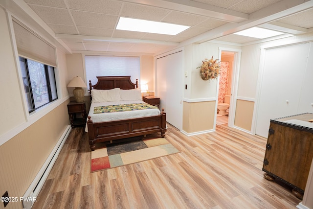 bedroom featuring a baseboard heating unit, light wood-type flooring, connected bathroom, and a paneled ceiling