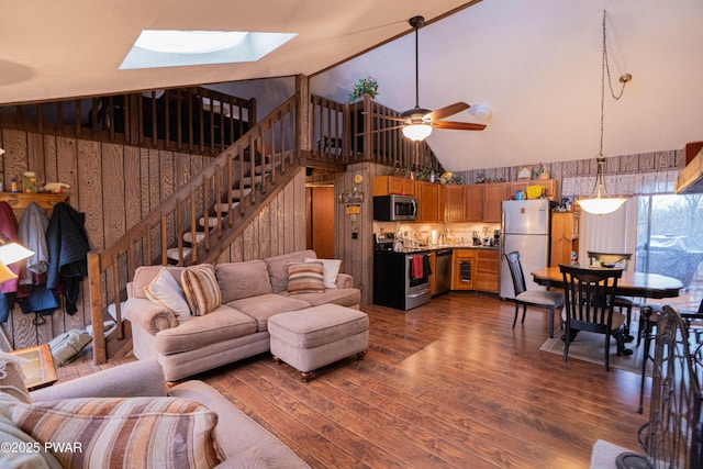 living area with dark wood-style floors, a skylight, stairway, ceiling fan, and wooden walls