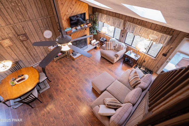 living area with lofted ceiling with skylight, wood-type flooring, ceiling fan, and wooden walls