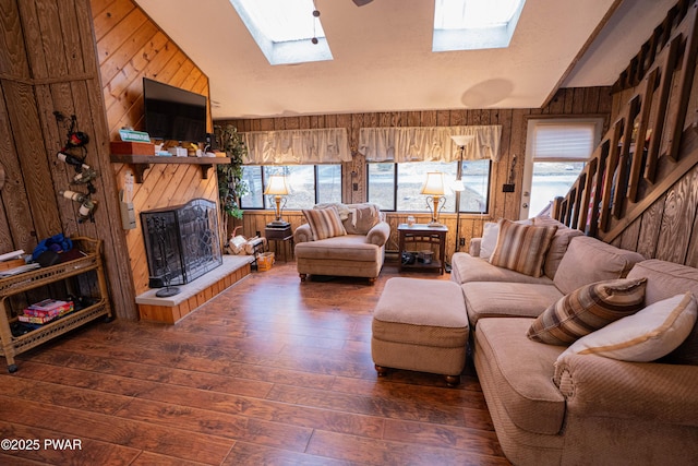 living room featuring lofted ceiling with skylight, wooden walls, a fireplace with raised hearth, and hardwood / wood-style floors