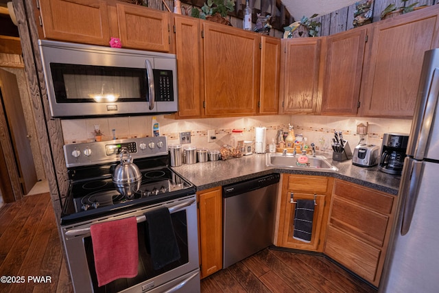 kitchen with dark wood-style floors, dark countertops, backsplash, appliances with stainless steel finishes, and a sink