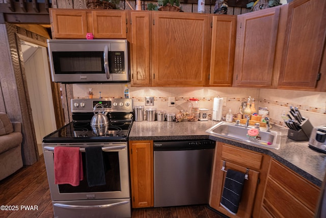 kitchen with dark wood-style flooring, dark countertops, decorative backsplash, appliances with stainless steel finishes, and a sink