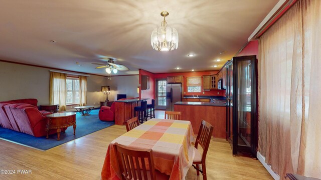 dining room with light hardwood / wood-style floors, ceiling fan with notable chandelier, and ornamental molding